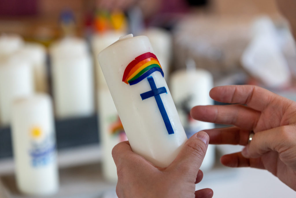 weiße Kerze mit einem Regenbogen und einem Kreuz